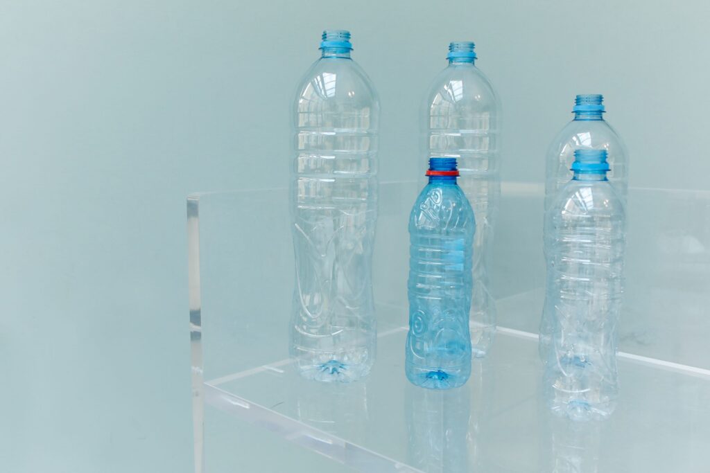 Five assorted empty plastic bottles displayed on a clear shelf with a soft blue background.
